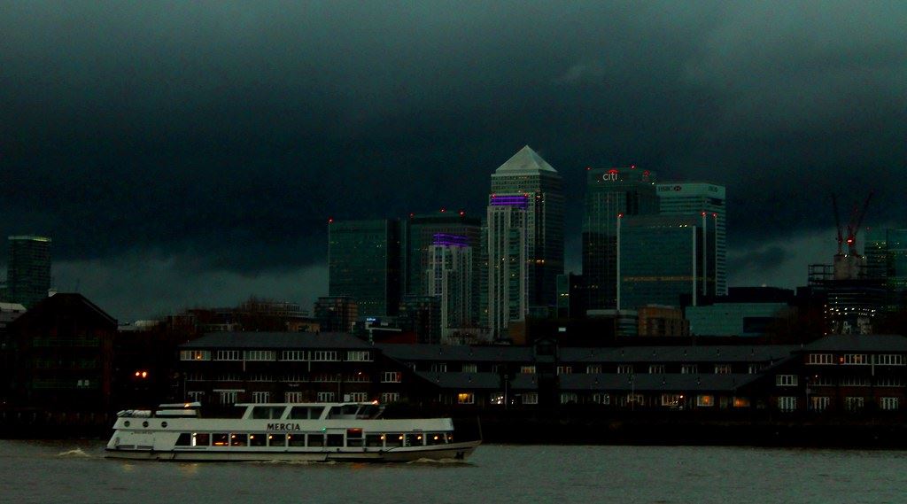 The Docklands skyline at dusk seen from the river, with office towers lit against a dark sky